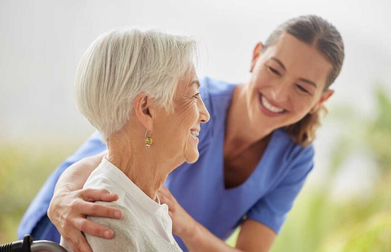 Staff member assists an older resident with a walker in a bright assisted living hallway.